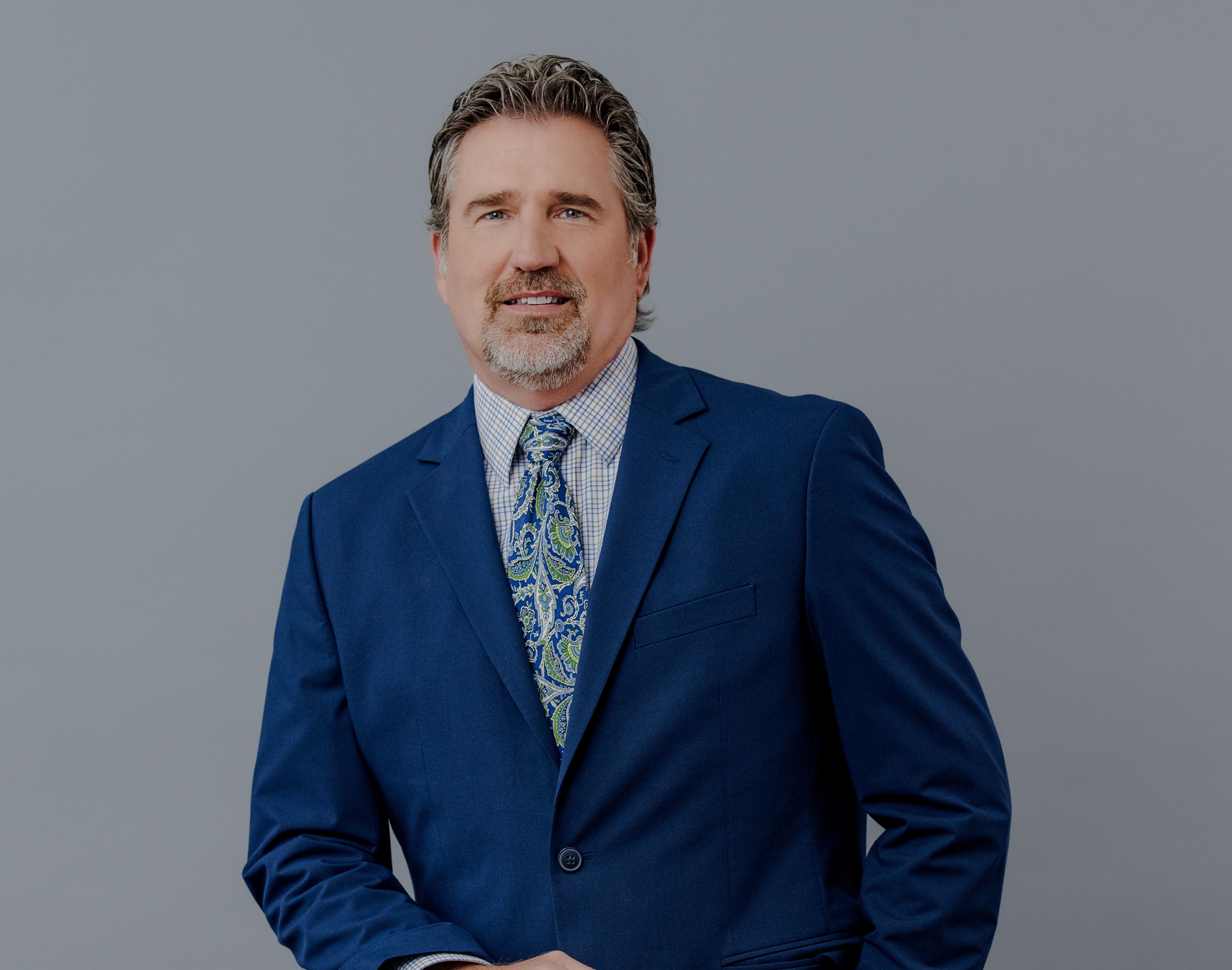 Headshot of a businessman in a suit and tie in front of gray backdrop. 